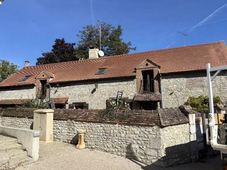 Maison en pierre et sa toiture en tuiles neuves, chantier de rénovation terminé