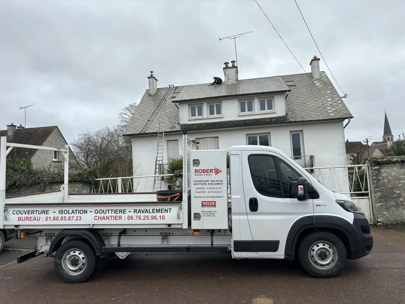 Camion Robert B. Couvreur devant une maison, réparation de toiture en cours sur le toit